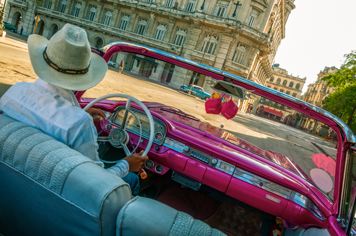 Taxi driver in a traditional hat driving a vintage car in Old Havana, Cuba.